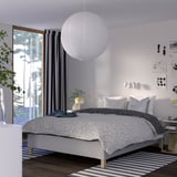 Modernt sovrum med sängen RISEHÖJDEN , vitprickiga sängkläder, stor taklampa, randig matta, stort fönster, gardiner, växter.