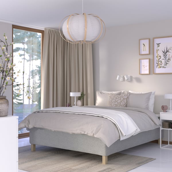 Minimalistiskt sovrum med sängen RISHÖJDEN , gråa sängkläder, rund ljusinsläpp, hörnblommor, konst, beige gardiner.