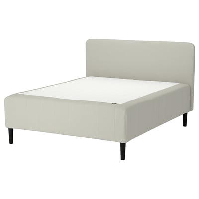 Modern säng med krämfärgat tyg, träben, sänggavel och tuftad design.