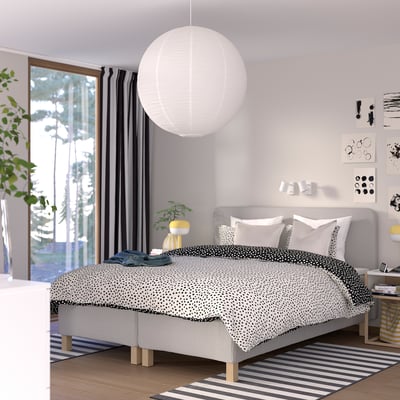 Modern säng, vit sänggavel, prickigt överkast, svarta gardiner, stor pendellampa, under fönstret.