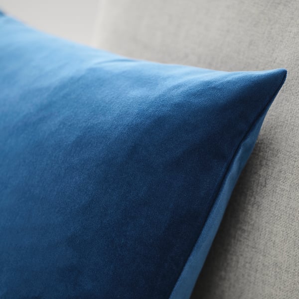 Närbild av ett mjukt, djupblått kuddfodral i sammet på en neutral soffa, som framhäver dess lyxiga struktur och kvalitet.