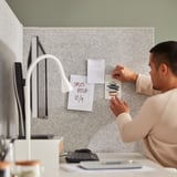 En person organiserar anteckningar på en bärbar rumsavdelare och använder den som en anslagstavla. I installationen ingår en dator och kontorsartiklar.