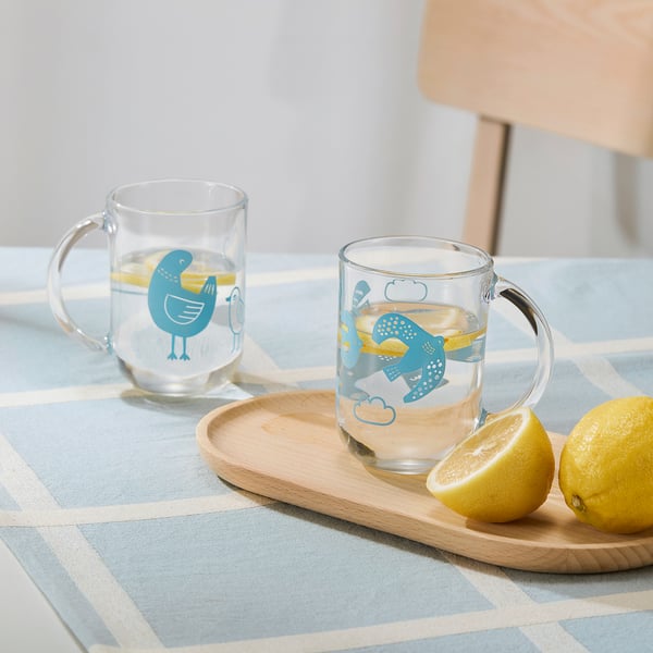 Blå fågelmuggar med citronvatten och halverad citron på ett blårutigt bord.