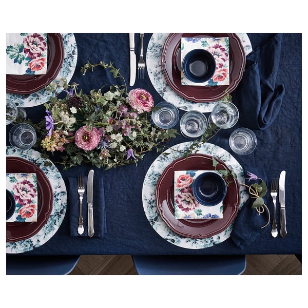 Elegant dukning med mörkblå tallrikar, blommiga servetter, glas, bestick och ett centralt blomsterarrangemang på blå duk.