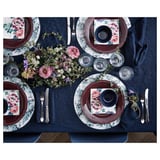 Elegant dukning med mörkblå tallrikar, blommiga servetter, glas, bestick och ett centralt blomsterarrangemang på blå duk.