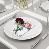 En dukning med en vit tallrik, blommig servett, ros, bestick och glas.