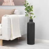 Ett minimalistiskt vardagsrum med en vit soffa, en beige prydnadskudde och filt och en stor svart dekorativ vas med gröna konstgjorda blommor.