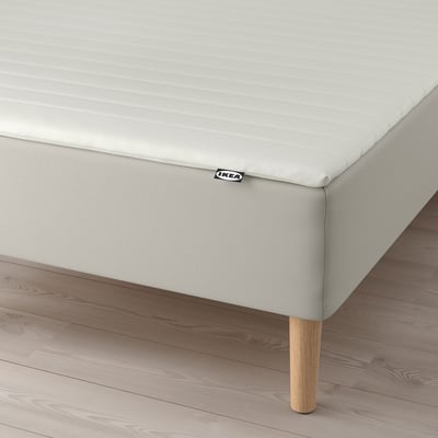 Stilren, modern säng med ljusgrå stoppad sänggavel, träben och vit madrass.