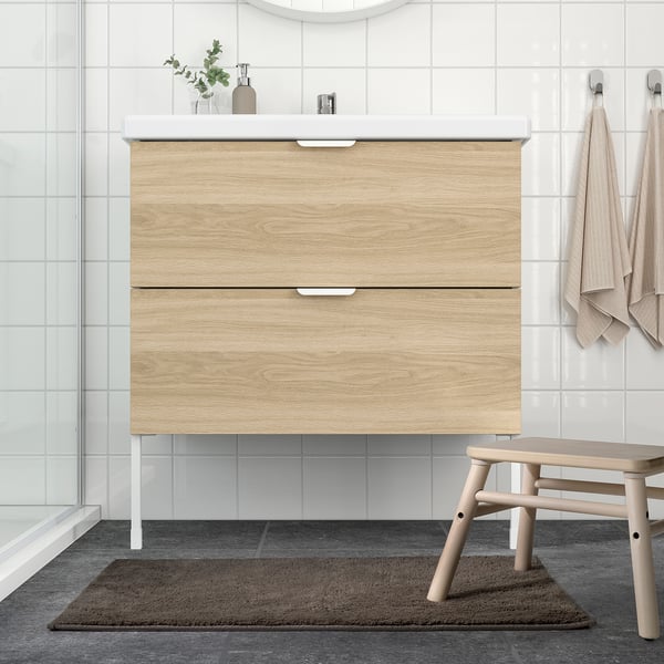 Modernt badrum med ljust handfat och brun badrumsmatta.
