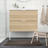Modernt badrum med ljust handfat och brun badrumsmatta.