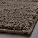 Närbild av en texturerad, plyschig badrumsmatta med tjock bomullslugg. Kanterna vikta över med en slät yta som avslöjar en mjuk, inbjudande yta.