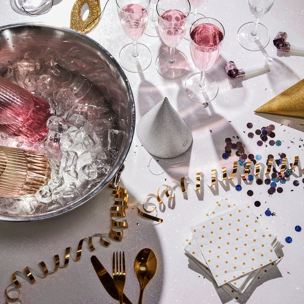 Champagne-ishink med namnet SOLDRÄNKT, glänsande silver, handtag för enkelhet, rymmer flera flaskor, omgiven av glas och festdekorationer.