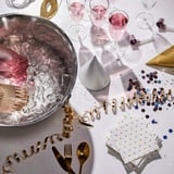 Champagne-ishink med namnet SOLDRÄNKT, glänsande silver, handtag för enkelhet, rymmer flera flaskor, omgiven av glas och festdekorationer.