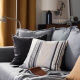 Ett modernt vardagsrum en grå soffa med flera kuddar, bland annat en randig i grått och beige, och en läderplånbok på den.