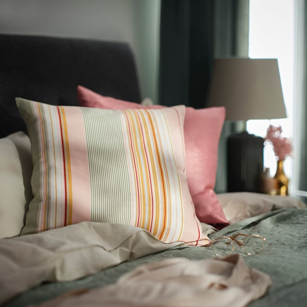 Ljust randig rosa och flerfärgad kudde på en säng, med en lampa bredvid.