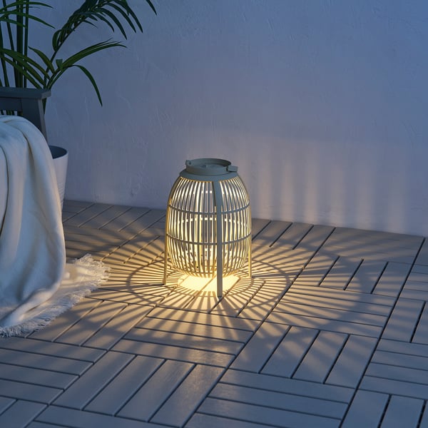 Grön SOLVINDEN golvlampa med rottingmönster på däck, upplyst med växt och tyg.