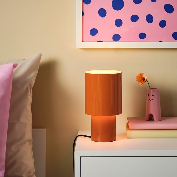 Orange lampa på ett litet bord, nära vasen med en orange blomma.