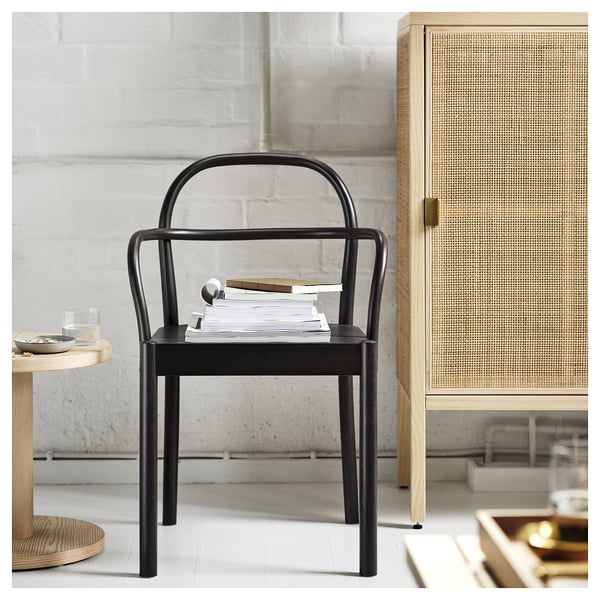 Modern svart matstol med trave böcker, bredvid träskåp och litet bord med klart glas.