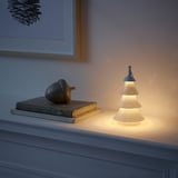 En liten, tänd trädformad lampa på en hylla, bredvid böcker och ett prydnadsföremål.