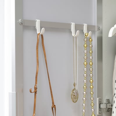 Vita krokar hänger bälten och halsband prydligt i en garderob, som är en del av förvaringssystemet STRAUMEN.