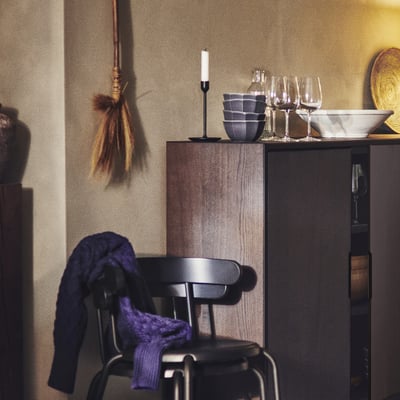 En mysig kökshörna med svarta stolar draperade med blått tyg, ett ljus och skålar på ett träbord och hängande inredning.