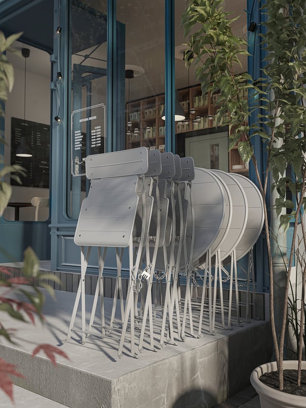 Staplade gråa SUNDSÖ metallstolar utanför modernt blått café. Stolsdesign enkel, hopfällbar, hållbar.