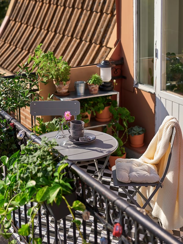 Balkonginredning med grått SUNDSÖ bord & stol, krukväxter, lykta och filt.