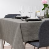 Bordsset med grå SVARTSENAP-duk, tallrikar, bestick, glas, karaff och blomvas.