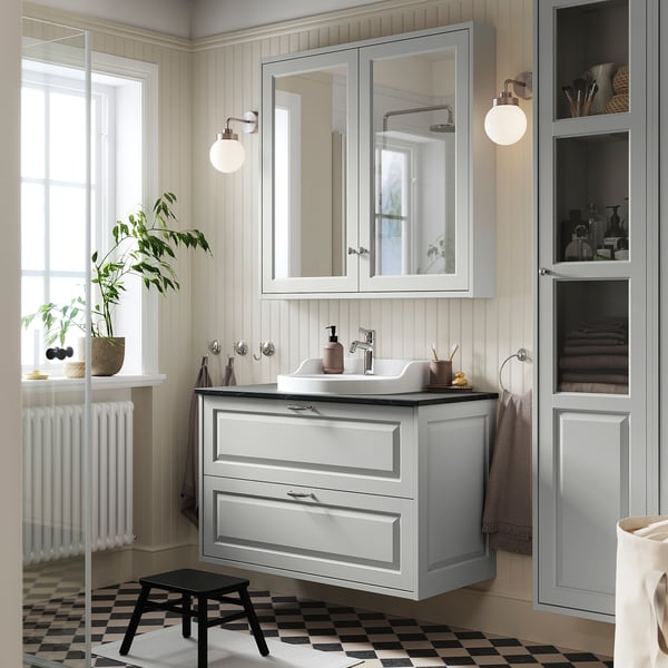 Modernt grått badrum med TÄNNFORSEN kommod, stor spegel och elegant handfat. Växter och handdukar dekorerar utrymmet.