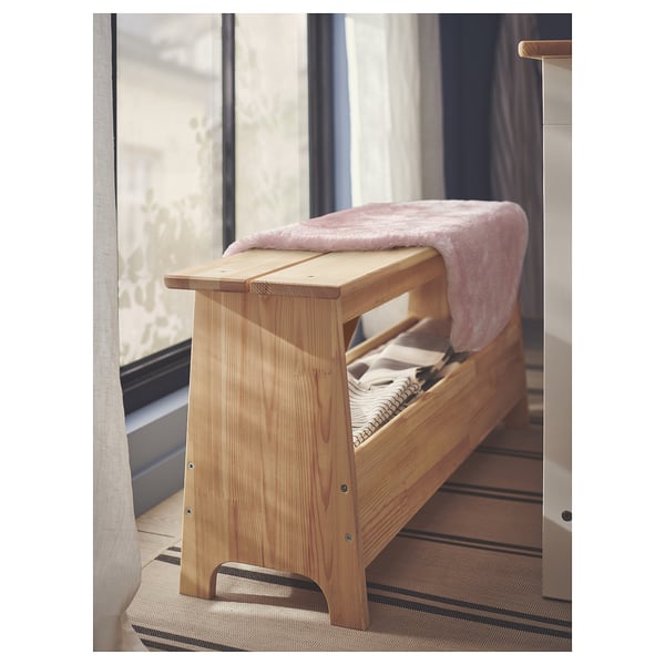 Träbänk med rosa lurvig filt, naturlig finish, enkel design, placerad nära ett fönster.