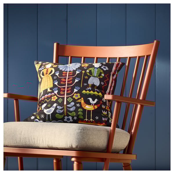 En knallorange stol med en färgglad dyna. Kudden visar en svensk folklig design i livfulla färger mot en mörk bakgrund.