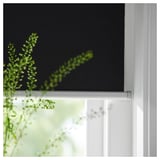 Svart rullgardin med en grön växt i fronten, monterad inuti en vit fönsterkarm, som visar upp TRETURs eleganta design.