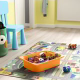 Orange leksaksbehållare med små fordon och figurer på färgrik lekmatta, blå barnstol nära.