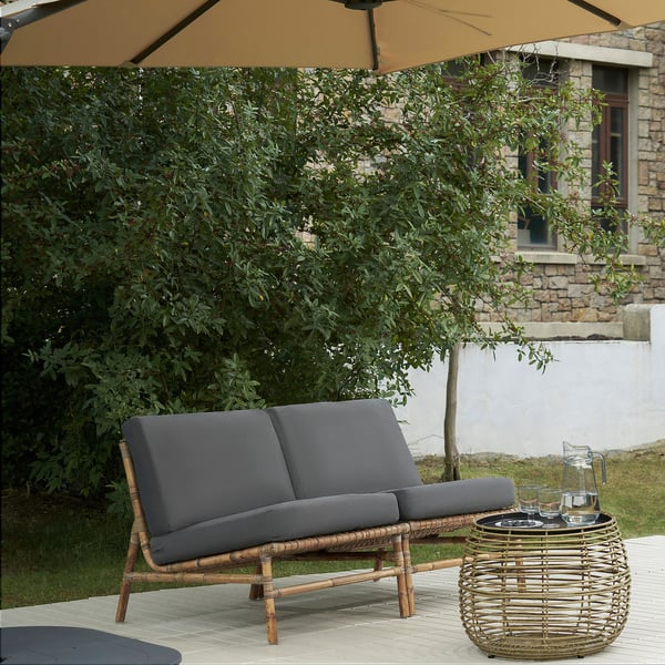 Grå vadderad loveseat med korgfot och bord, paraply.