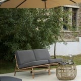 Grå vadderad loveseat med korgfot och bord, paraply.
