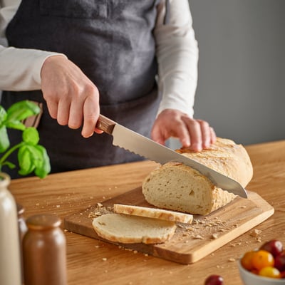 Person som skär bröd med en tandad kniv på en skärbräda av trä.