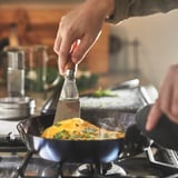 Matlagningsomelett i non-stick kolstålspanna på gasspis.