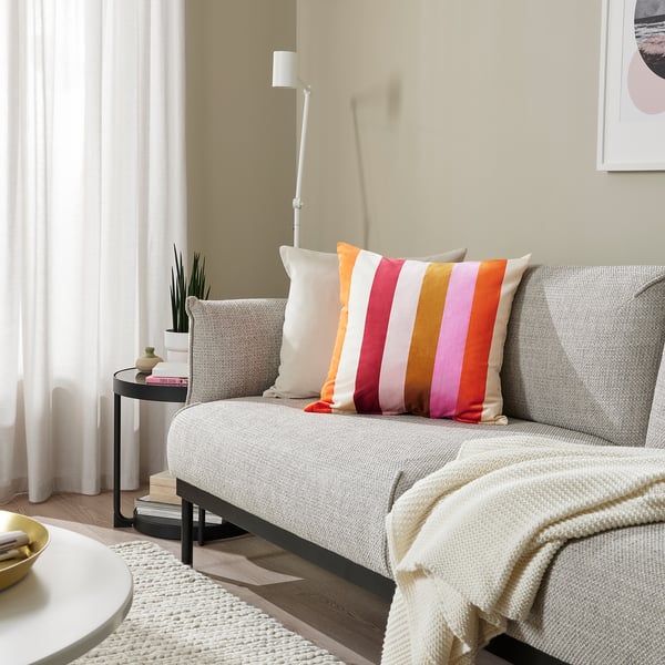 Mysigt vardagsrum med grå soffa, färgglad randig VATTENVÄN-kudde, sidobord och matta.