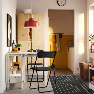 Modern kök med svarta hopfällbara stolar, träbord, röd pendellampa och hyllor. Gult kaklat kök med vita väggar.