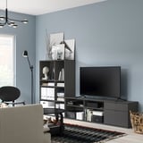 Modernt vardagsrum med blå väggar, svart tv-möbel, vit fåtölj, randig matta och golvlampa.