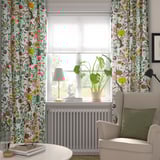 Mysig hörna med blommiga gardiner, fåtölj, växt och lampa.