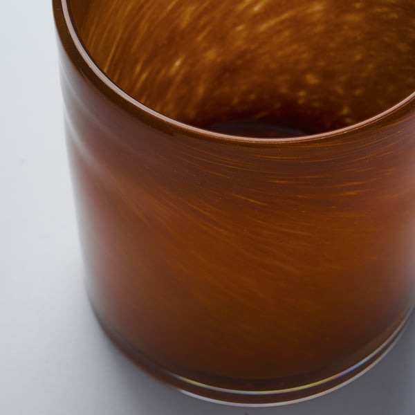 En närbild av en handgjord ljusstake i glas som visar dess släta, rödbruna yta och subtila mönster.