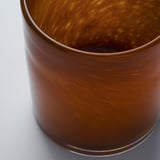 En närbild av en handgjord ljusstake i glas som visar dess släta, rödbruna yta och subtila mönster.