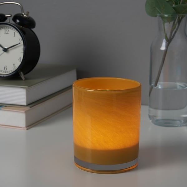 Ljusstake i orange glas på bordet, bredvid böcker och väckarklocka.