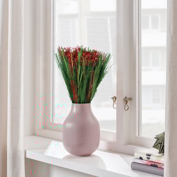 En bukett röda torkade blommor i en rosa vas står på en fönsterbräda och visar upp fräsch och festlig inredning.