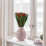 En bukett röda torkade blommor i en rosa vas står på en fönsterbräda och visar upp fräsch och festlig inredning.