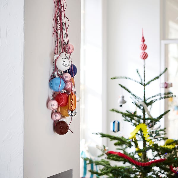 Färgglada VINTERFINT-kulor hänger: röd, blå, rosa, orange; vissa djurformade, större än träd.