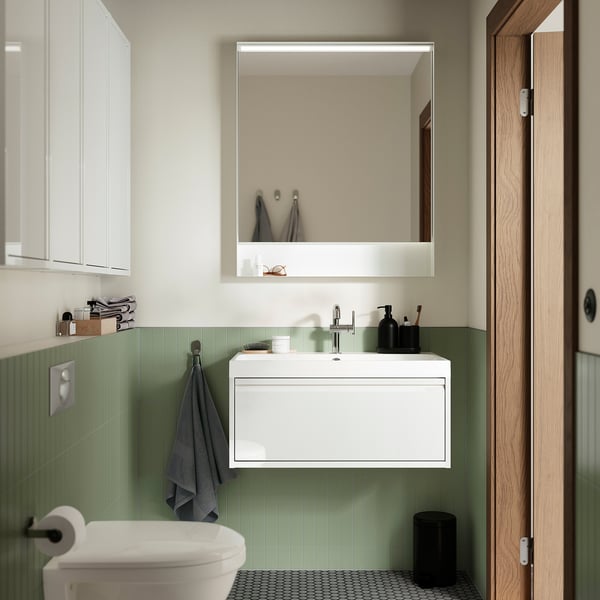 Modern bathroom with white floating white sink, green tiled wall, grey towel, mirror, toilet.