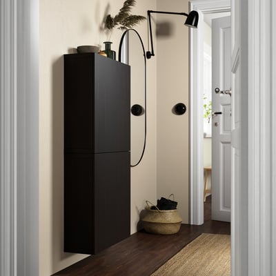 Modern hallway with tall black BESTÅ cabinet. Wall-mounted light. Woven basket at bottom, next to door.