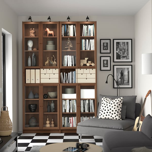 Large wooden BILLY bookshelf against white wall, grey sofa with polka dot pillow, numerous books, decorative items, photos.